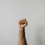 A person's arm raised with a clenched fist against a plain light background