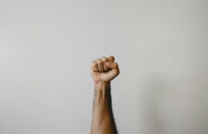 A person's arm raised with a clenched fist against a plain light background