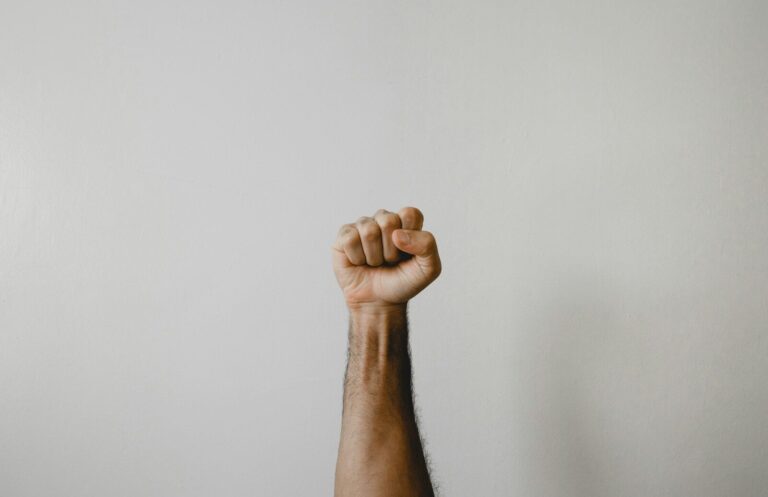 A person's arm raised with a clenched fist against a plain light background